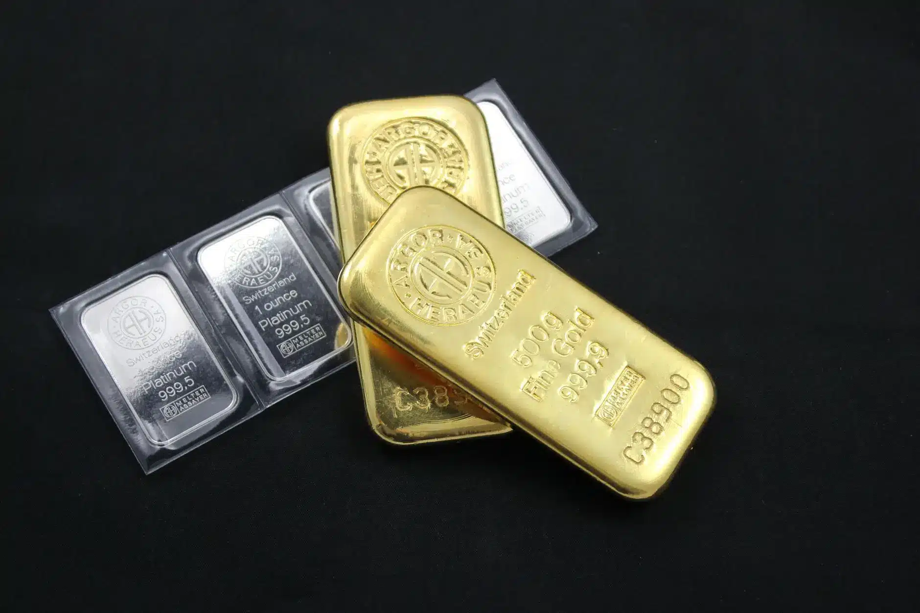 Shiny gold bullion bars alongside platinum bars on a dark background.