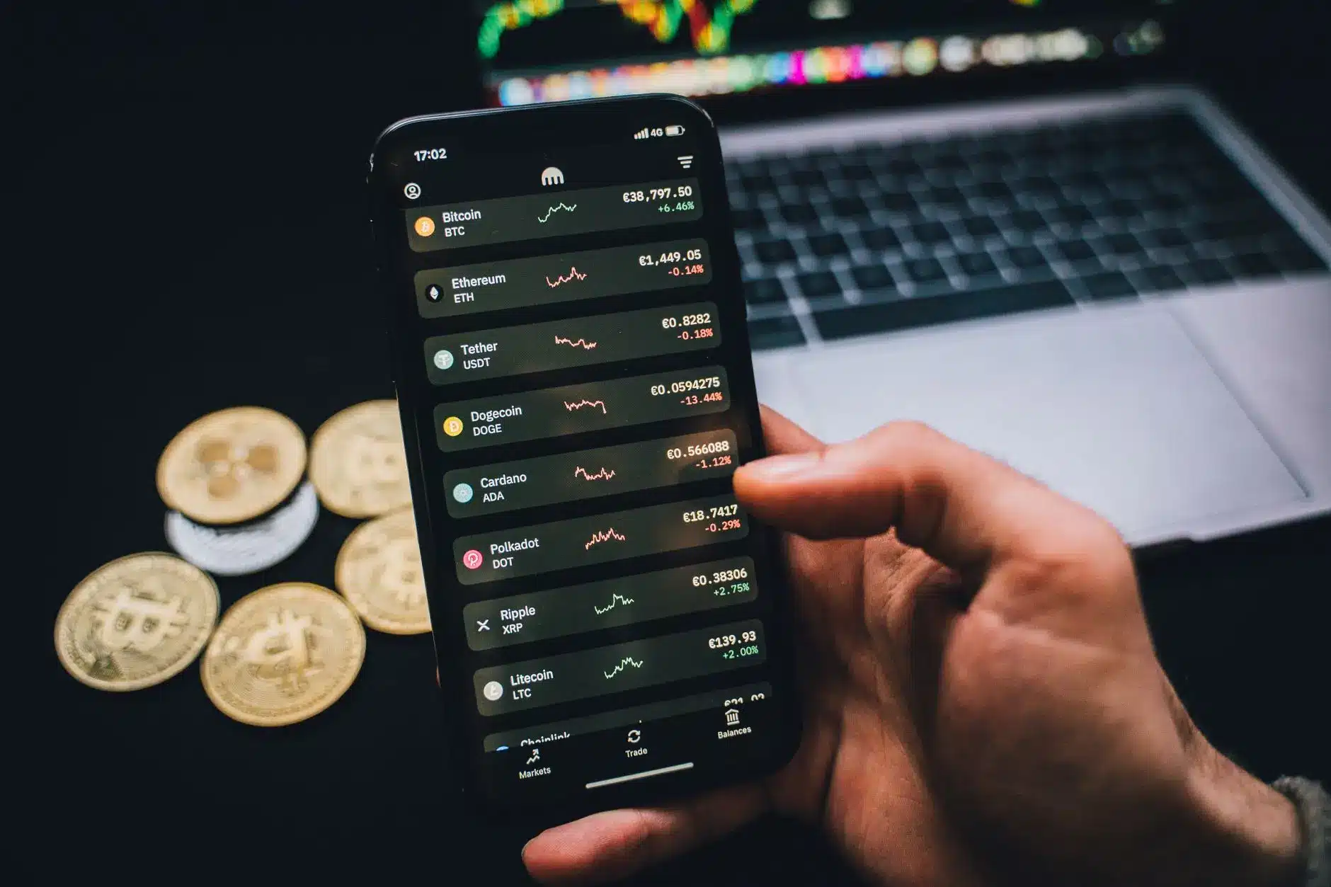 Close-up of a smartphone displaying crypto prices with gold coins in the background.